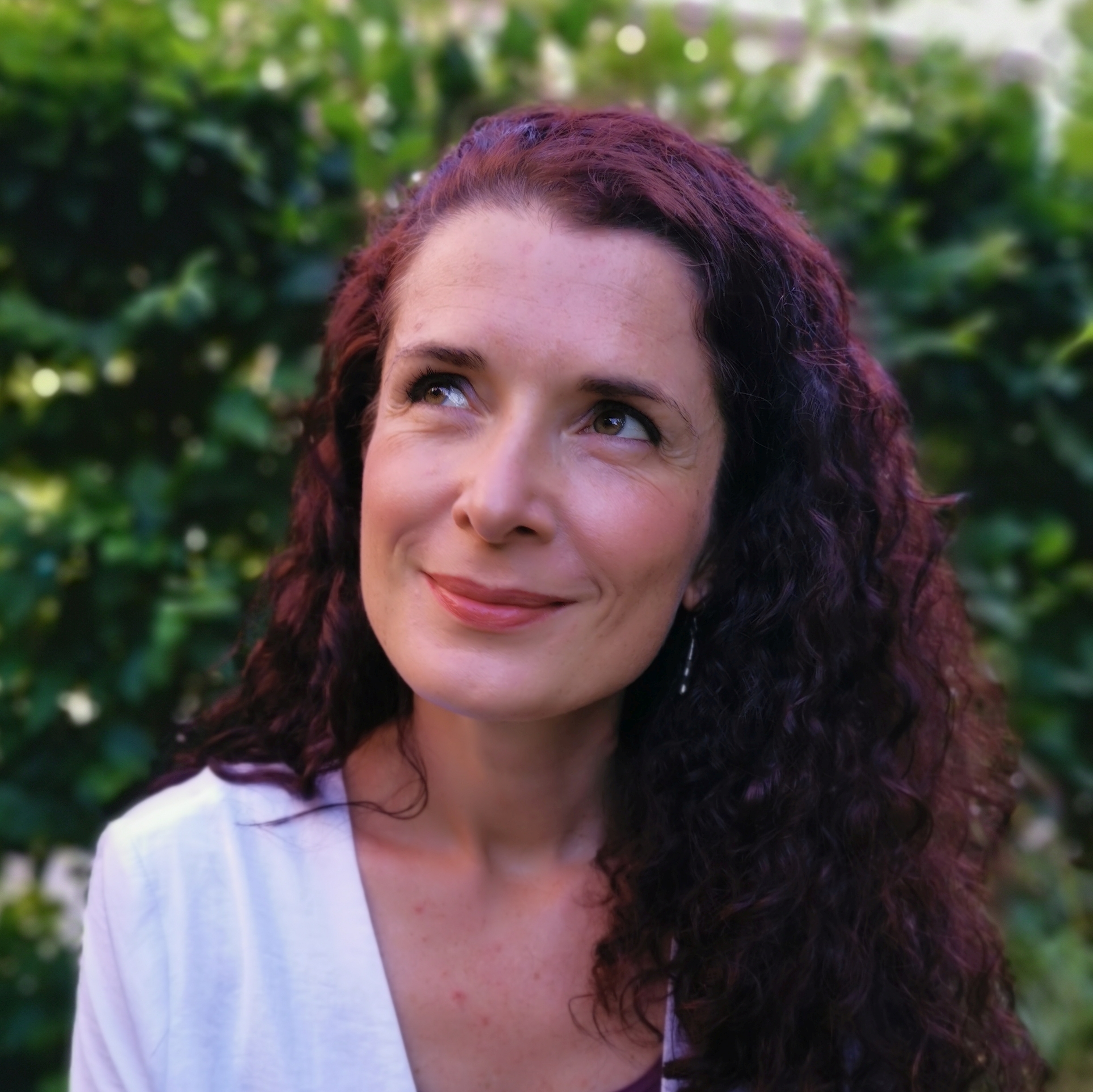 Portraitfoto von Diversity-Autorin und Verlegerin Karin Beese, lächelnd vor einer grünen Hecke mit Blick nach oben
